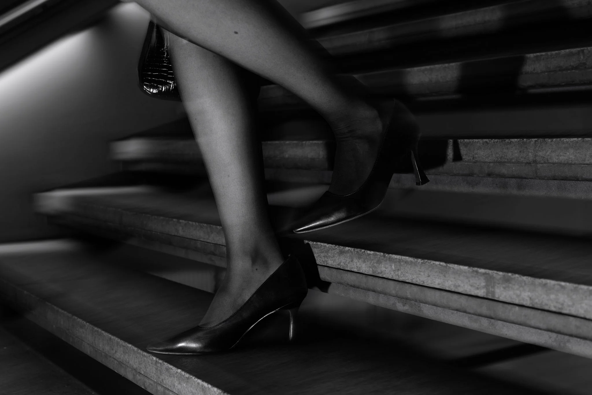 A woman’s foot in a high heel shoe on staircase steps, black and white photo.