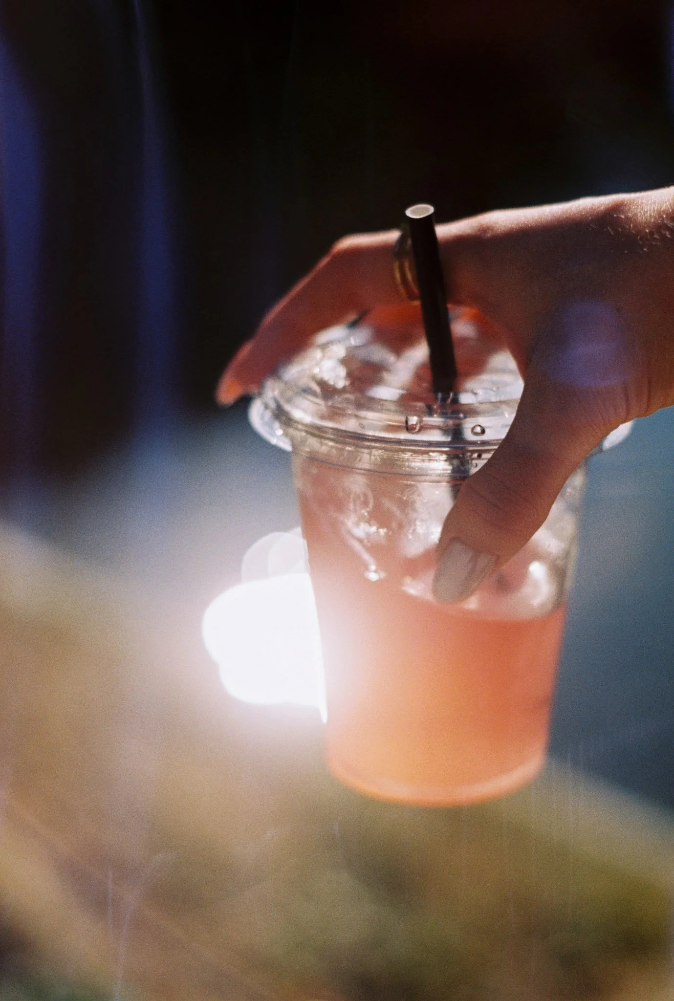 Person holding a plastic cup with iced beverage and a black straw.