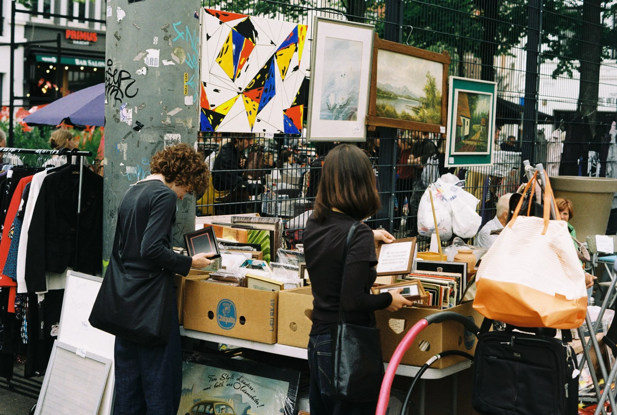 People browsing booths at an outdoor street market with artwork, paintings, and framed pictures on display.