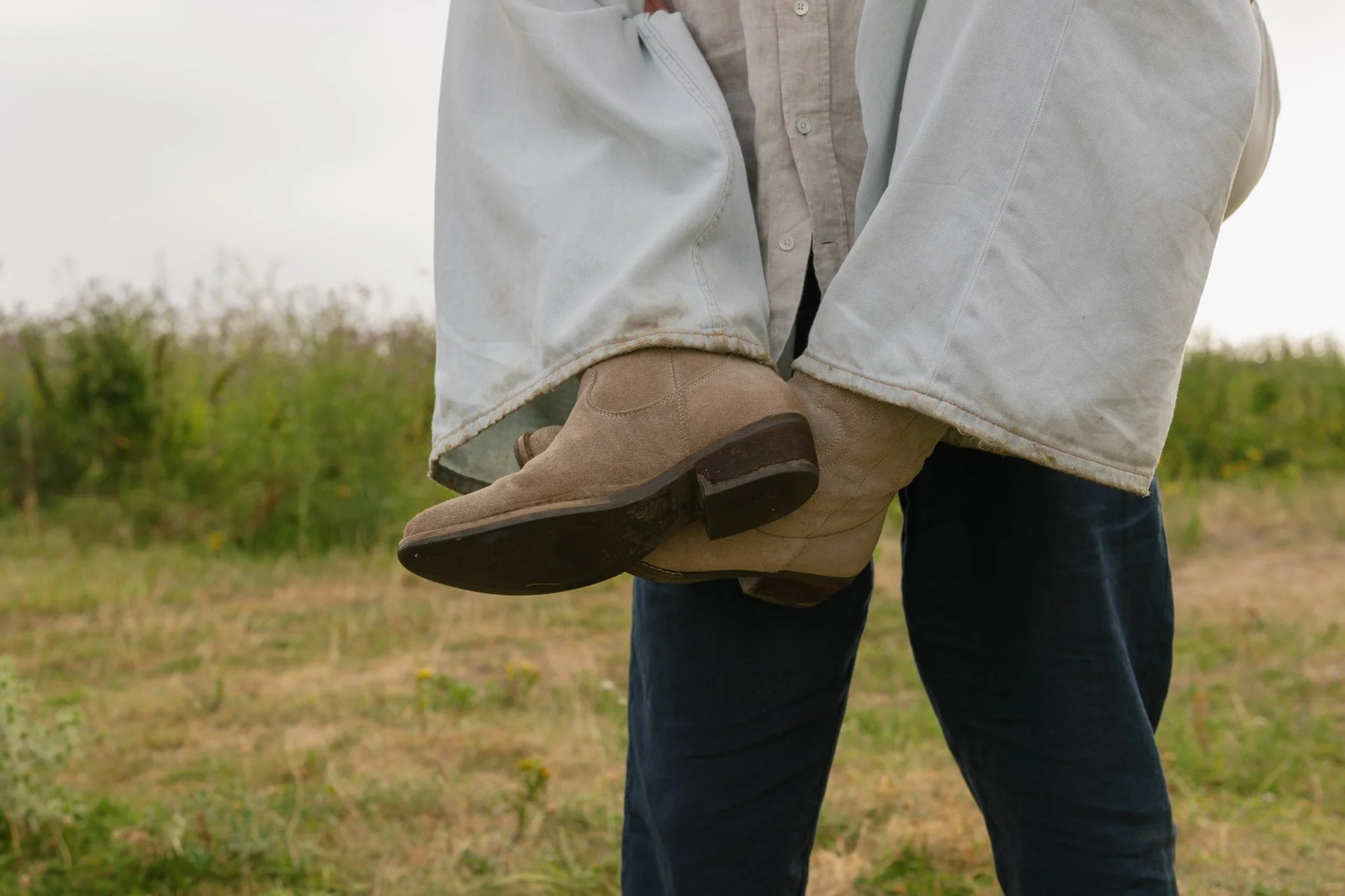 Person holding a child's leg while walking outdoors in a field.