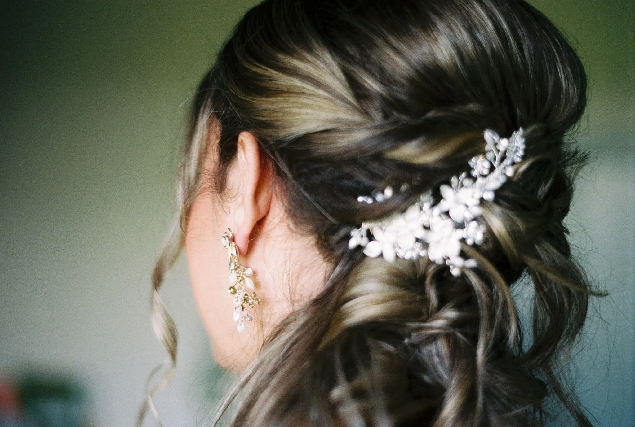 Close-up of a woman with styled hair adorned with a decorative hairpiece, wearing earrings, with a blurred green background.