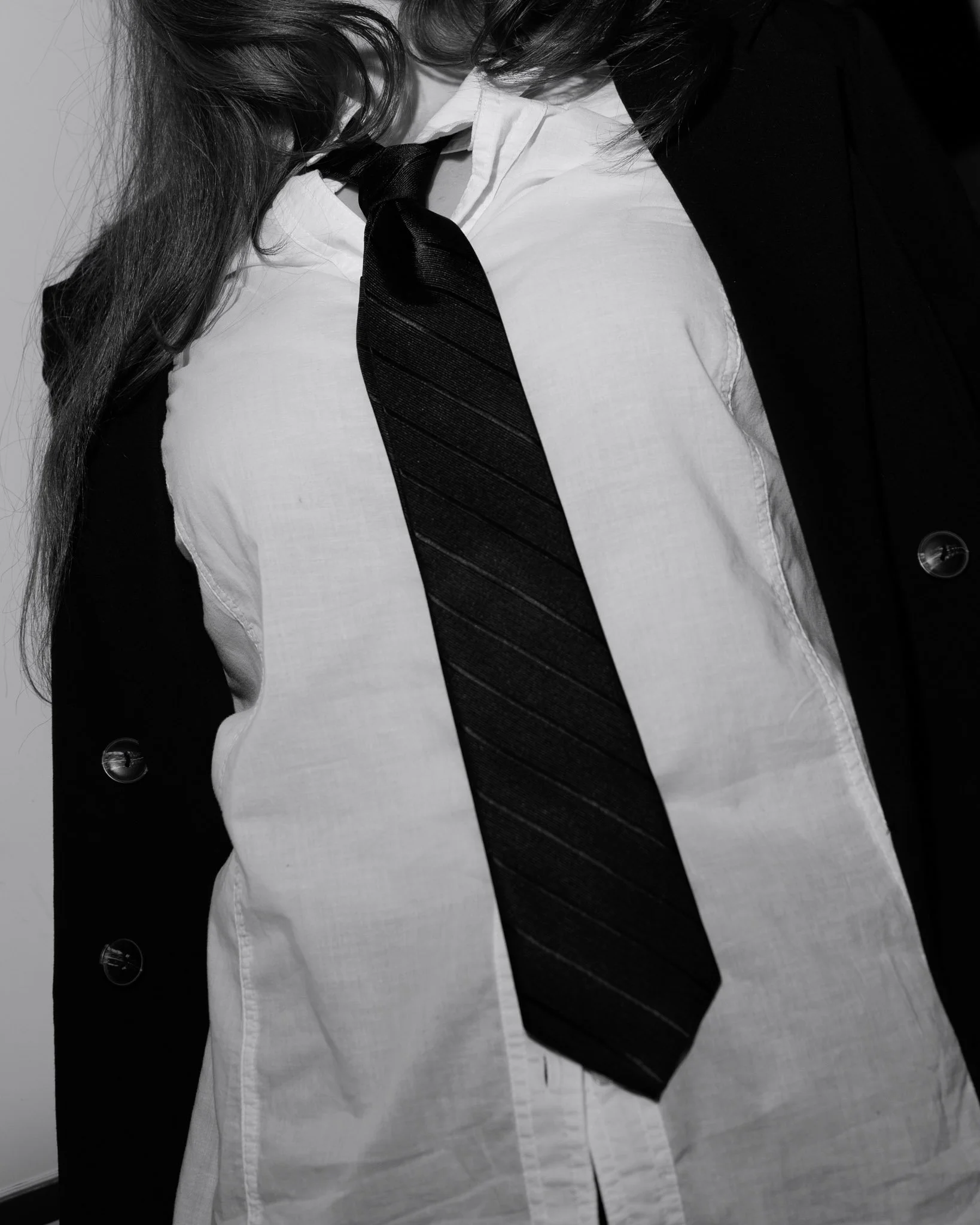 Close-up black and white photograph of a woman wearing a white shirt, black tie, and black cardigan, with long hair.