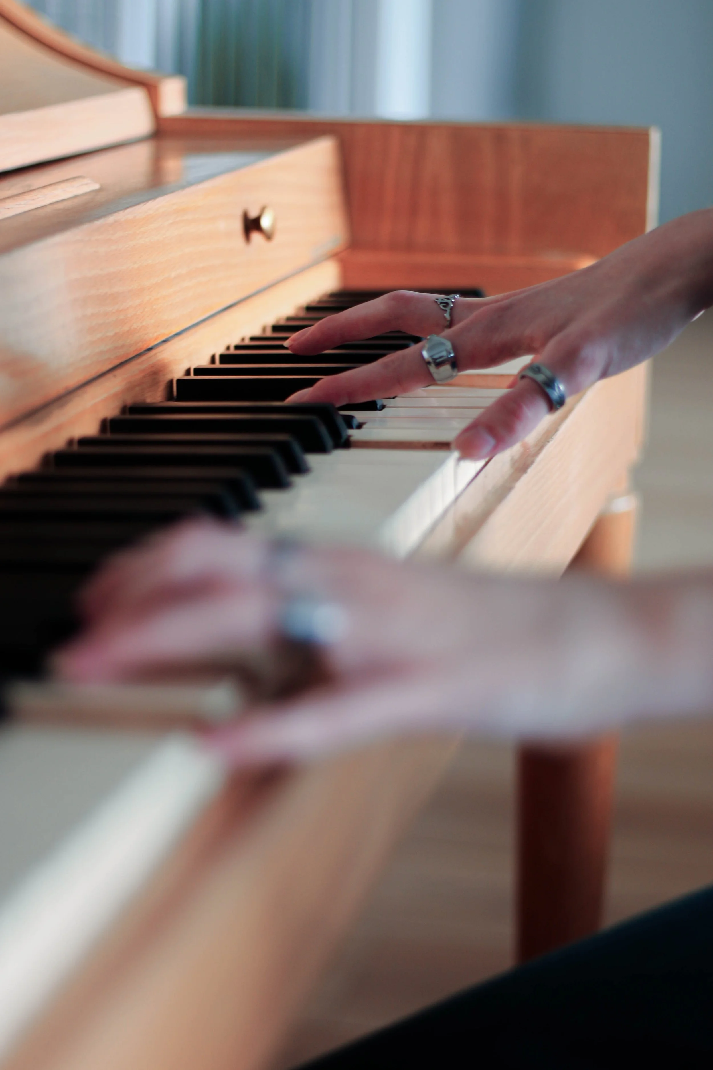 Close-up of a person's hand with rings playing a wooden upright piano.