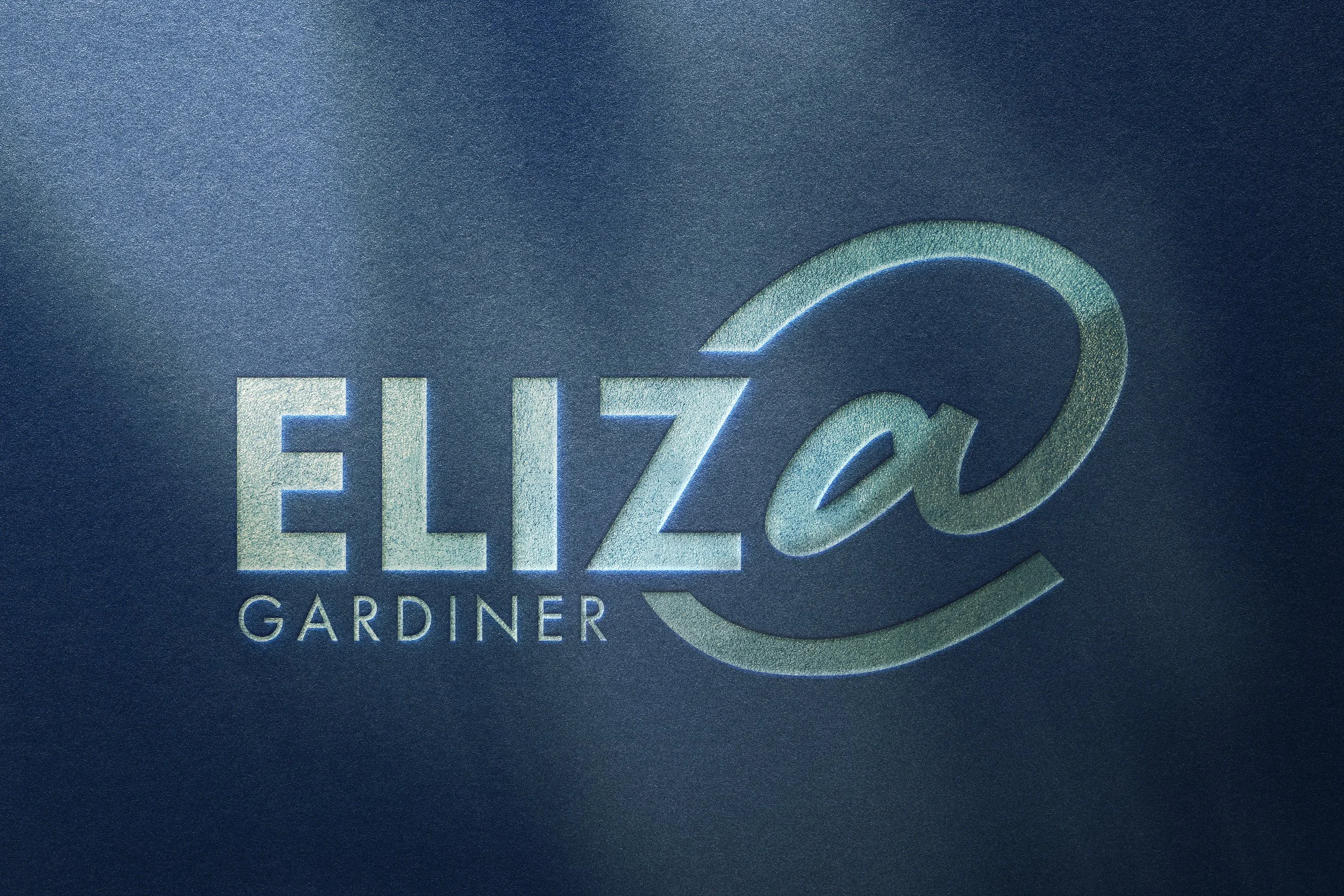 Close-up of a textured logo for Eliza Gardiner with a stylized 'A'  on a dark background.