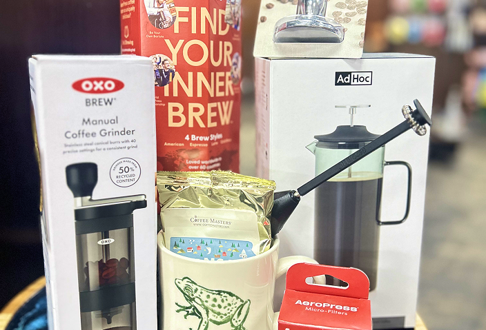A collection of coffee brewing items, including an OXO manual coffee grinder, a bag of Coffee Masters coffee, a small frog-themed mug, an Ad Hoc pour-over coffee maker, and a box of AeroPress micro-filters.