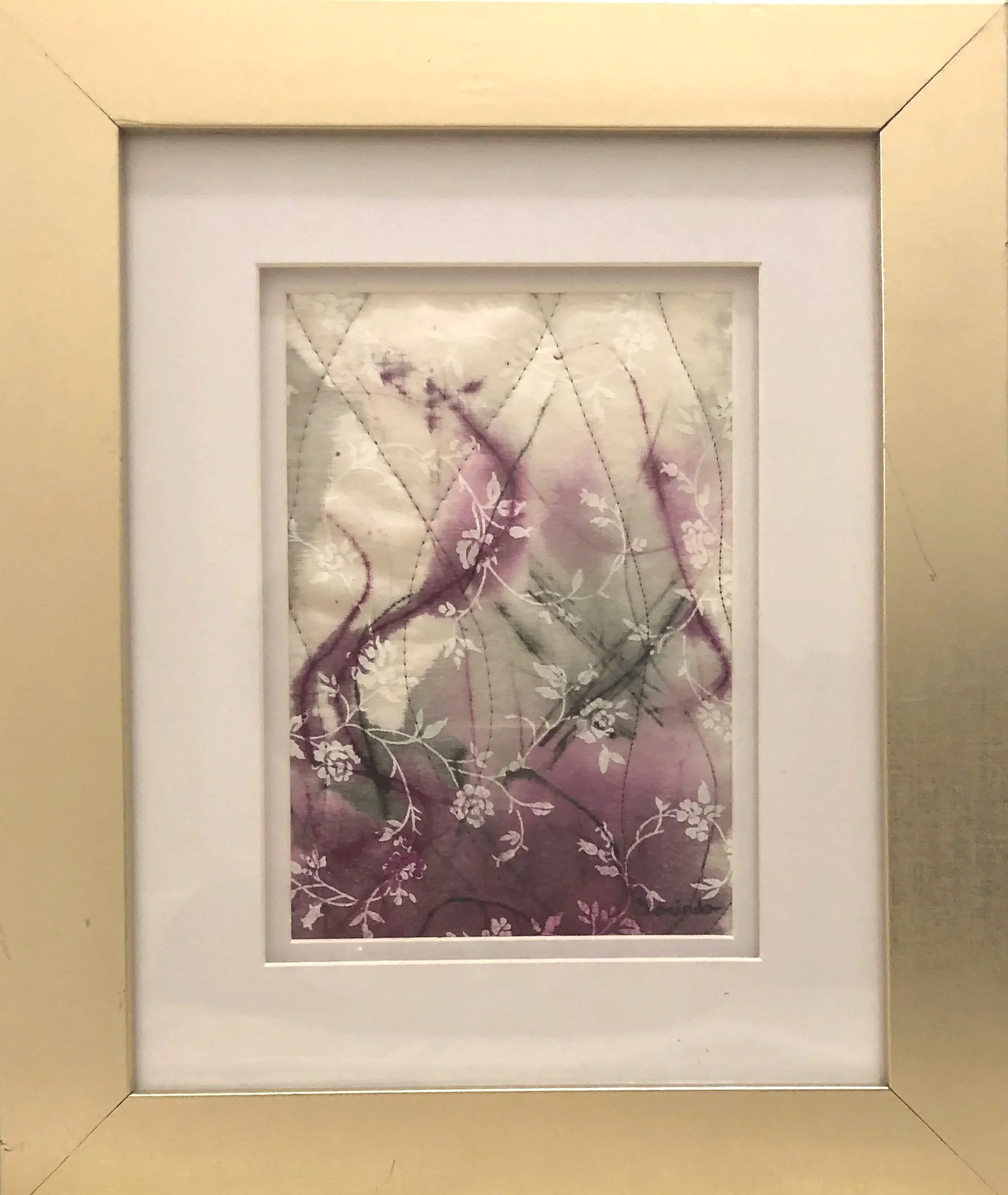 A framed wall art piece featuring a purple and white floral pattern with branches, within a white matting and a gold frame.