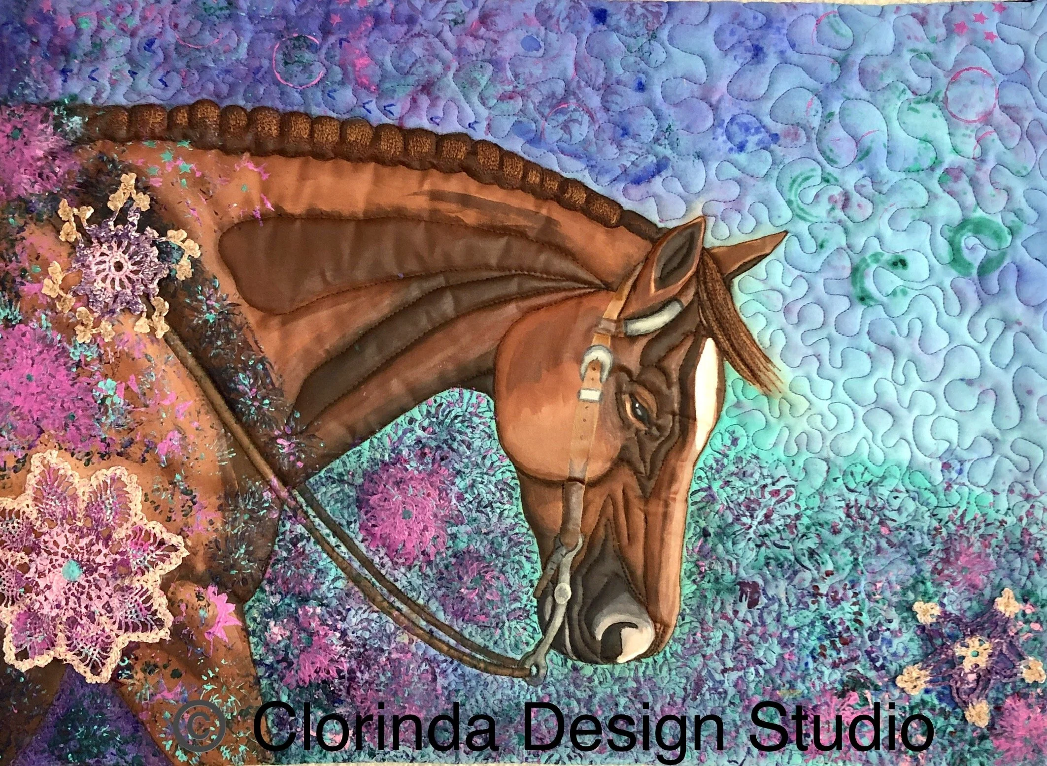 A colorful art quilt featuring a horse design, with abstract purple, blue, green, and pink patterns and sections of floral lace decoration.
