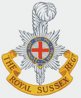 Coat of arms of the Royal Sussex Regiment featuring a cross with a crown and ribbon with motto 'The Royal Sussex Regt'.