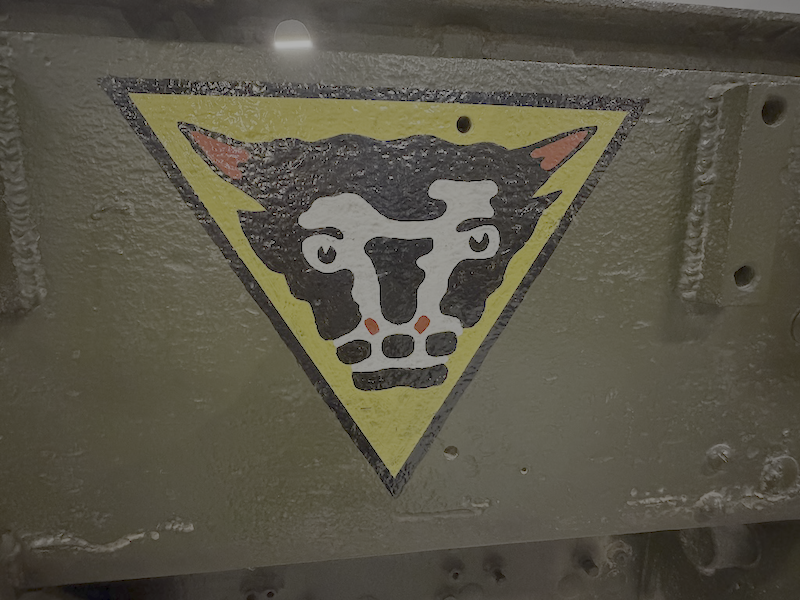 Painted warning sign of a cow's face inside a yellow triangle on a gray surface.