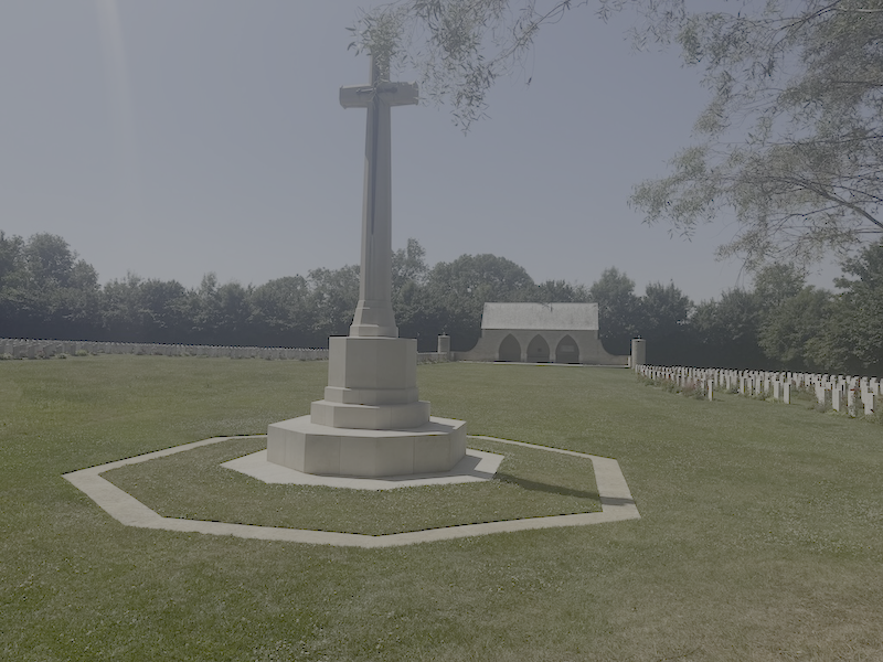 Gravestone with a large cross monument in a cemetery with rows of smaller grave markers in the background