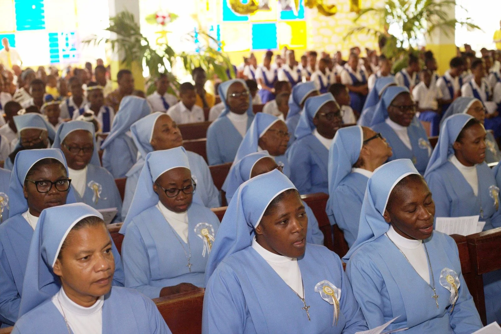 Group of nuns dressed in blue habits seated inside a church during a religious service.
