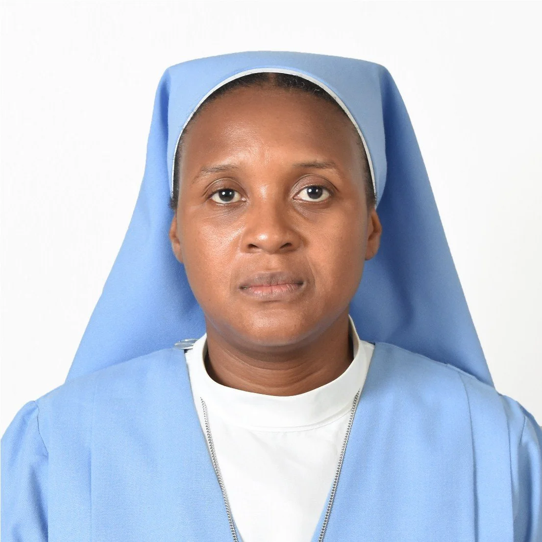 Close-up of a woman dressed as a nurse or nun, wearing light blue attire and a matching head covering, against a plain white background.