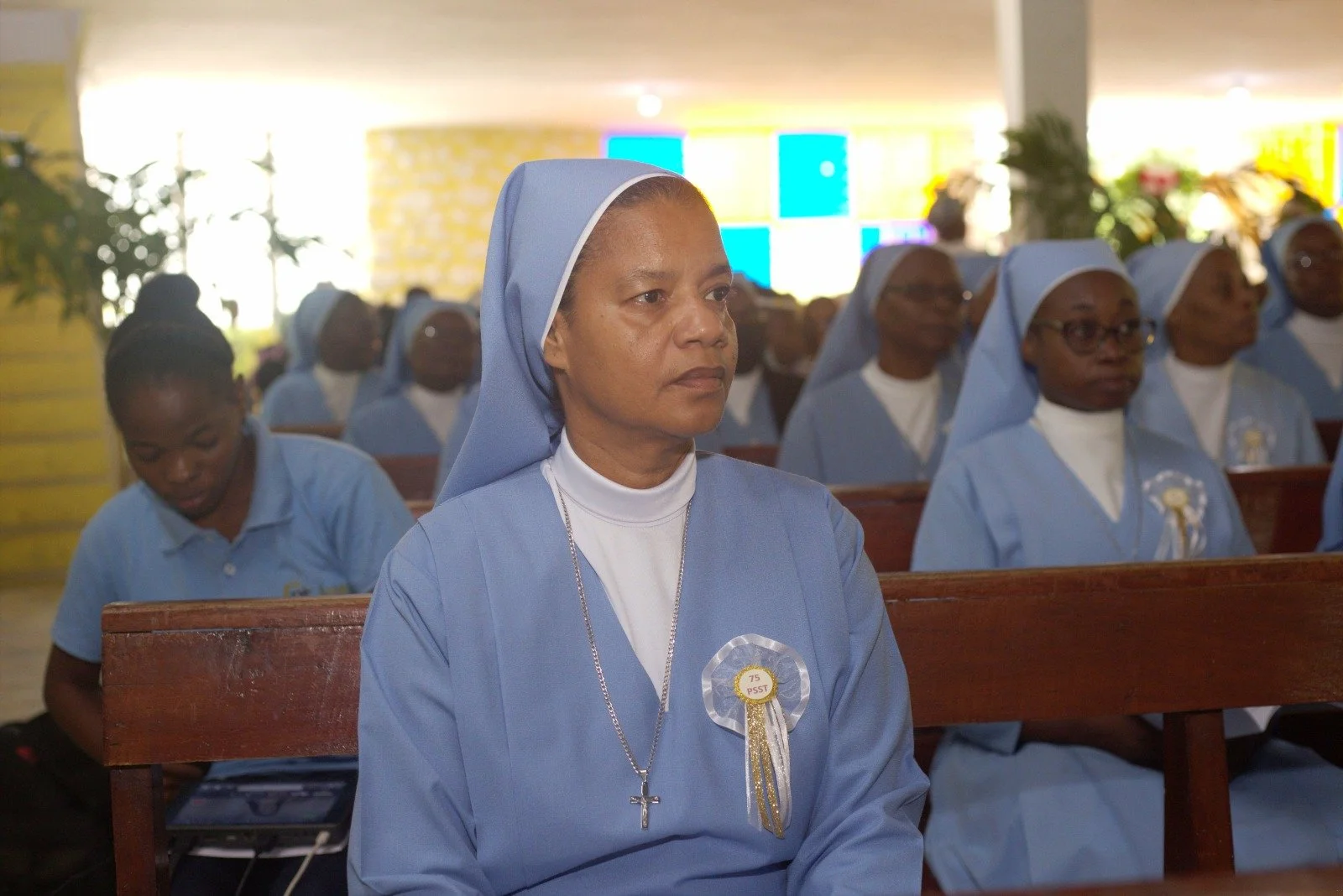 A group of nuns in light blue habits seated inside a church, attending a religious event or service.