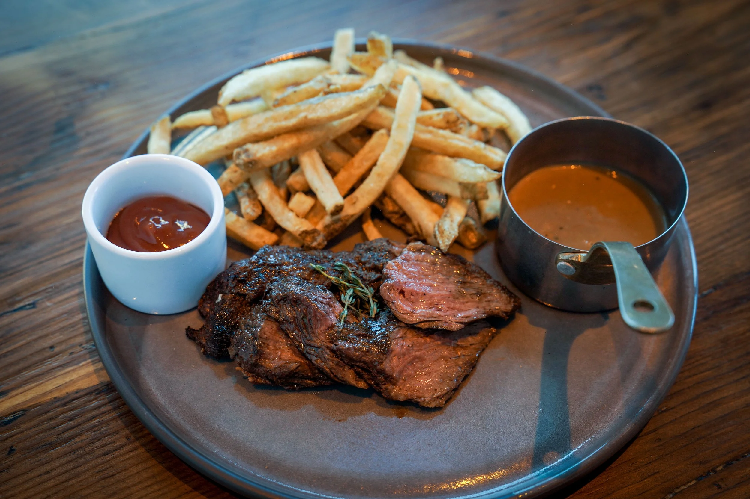 A plate of French fries, BBQ sauce, and sliced beef with gravy on a wooden table.