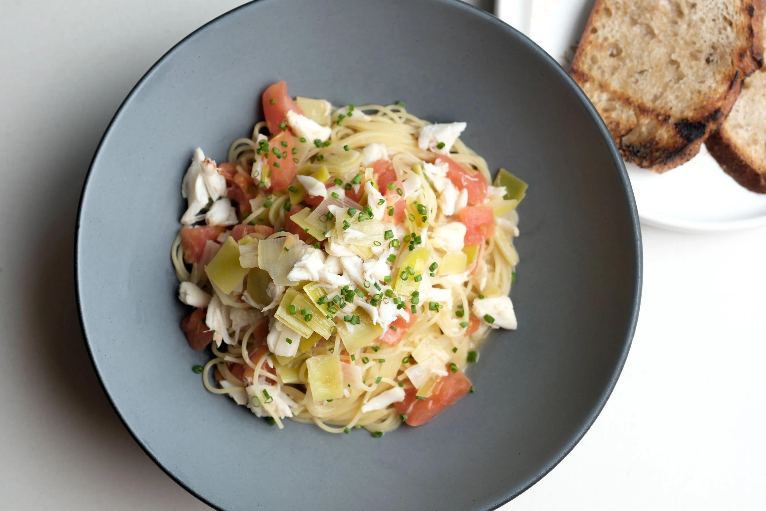 A bowl of spaghetti with chopped vegetables and shredded chicken, served with toasted bread slices on the side.
