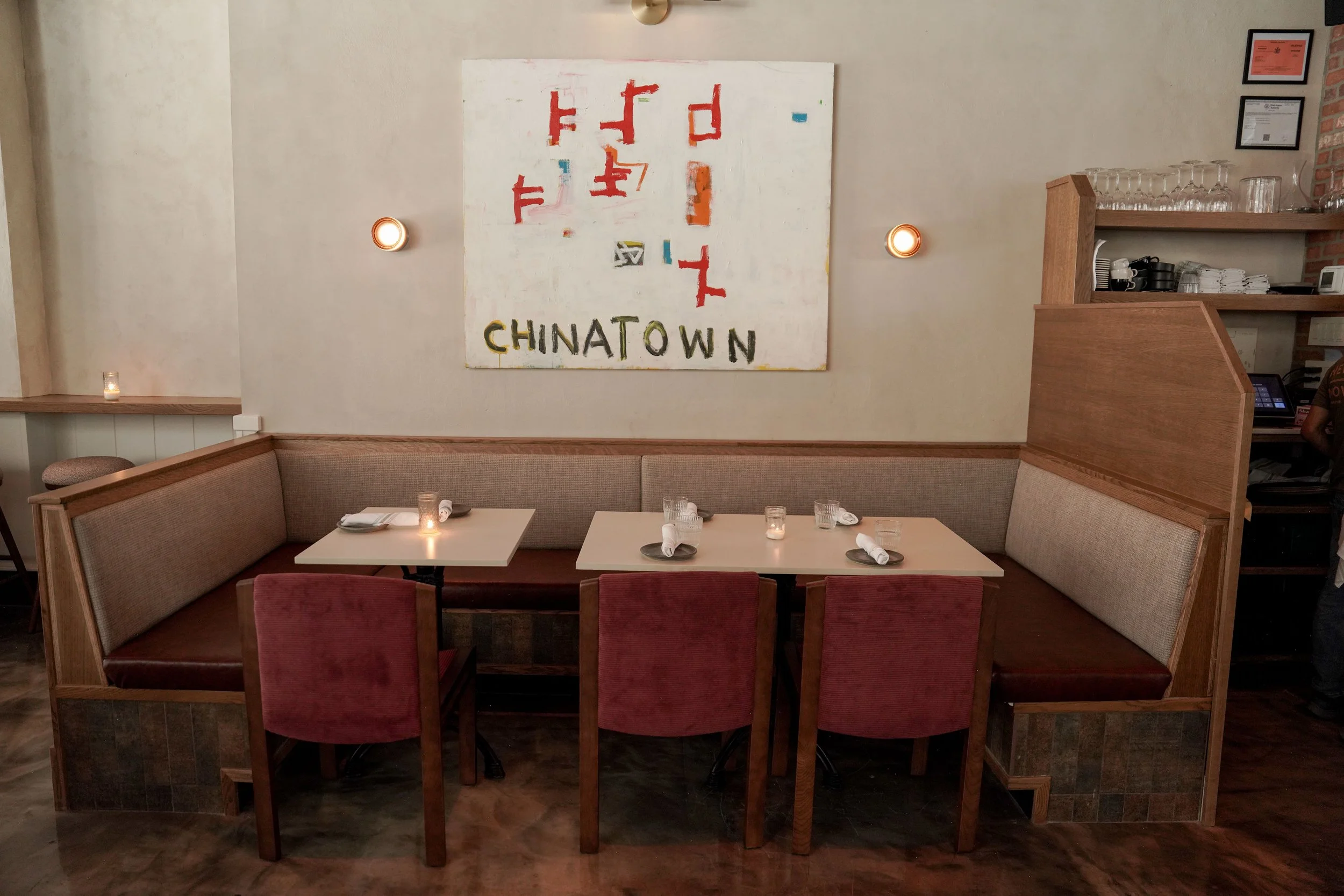 A cozy restaurant corner with a booth seating area, a wall art piece saying 'CHINATOWN', and a bar area with glassware and certificates on the wall.