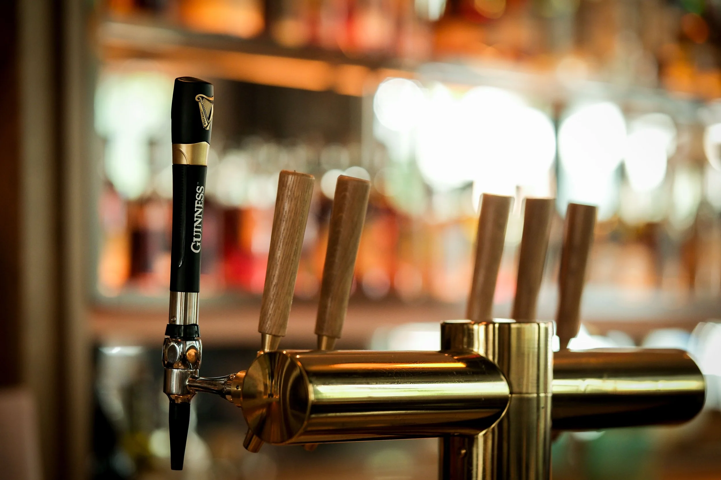 Tap handle on a beer tap dispenser, with several wooden handle taps nearby, in what appears to be a bar or pub setting.