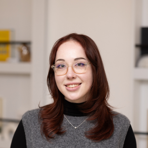 A woman with glasses and reddish-brown hair smiling in an indoor setting.