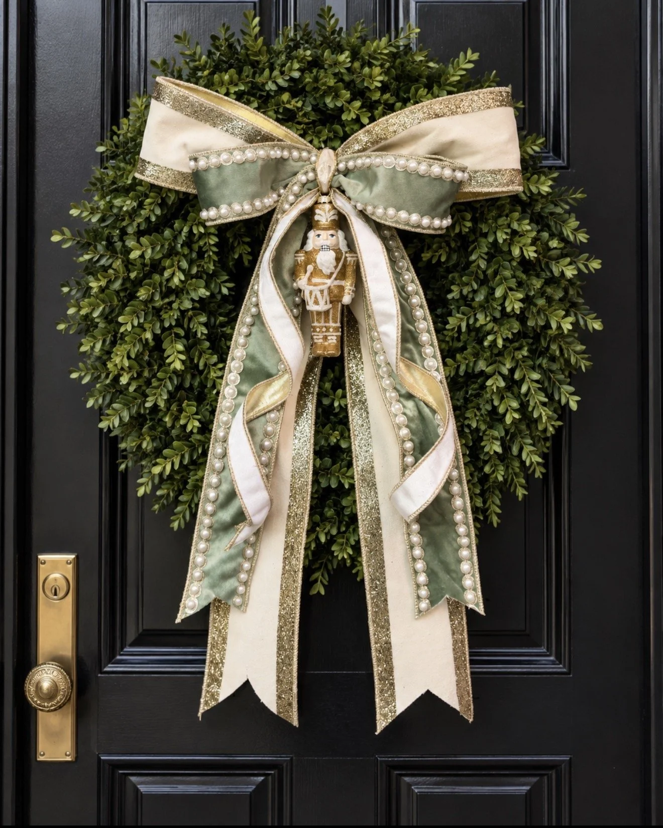 Elegant statement bow featuring soft sage velvet, ivory and shimmering gold ribbon, pearl-trimmed details, and a jeweled Nutcracker ornament charm . Bow has cascading tails. Holiday door statement.