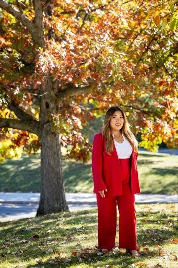 Photo of Tiffany in a red pant suit standing in front fall-colored trees.