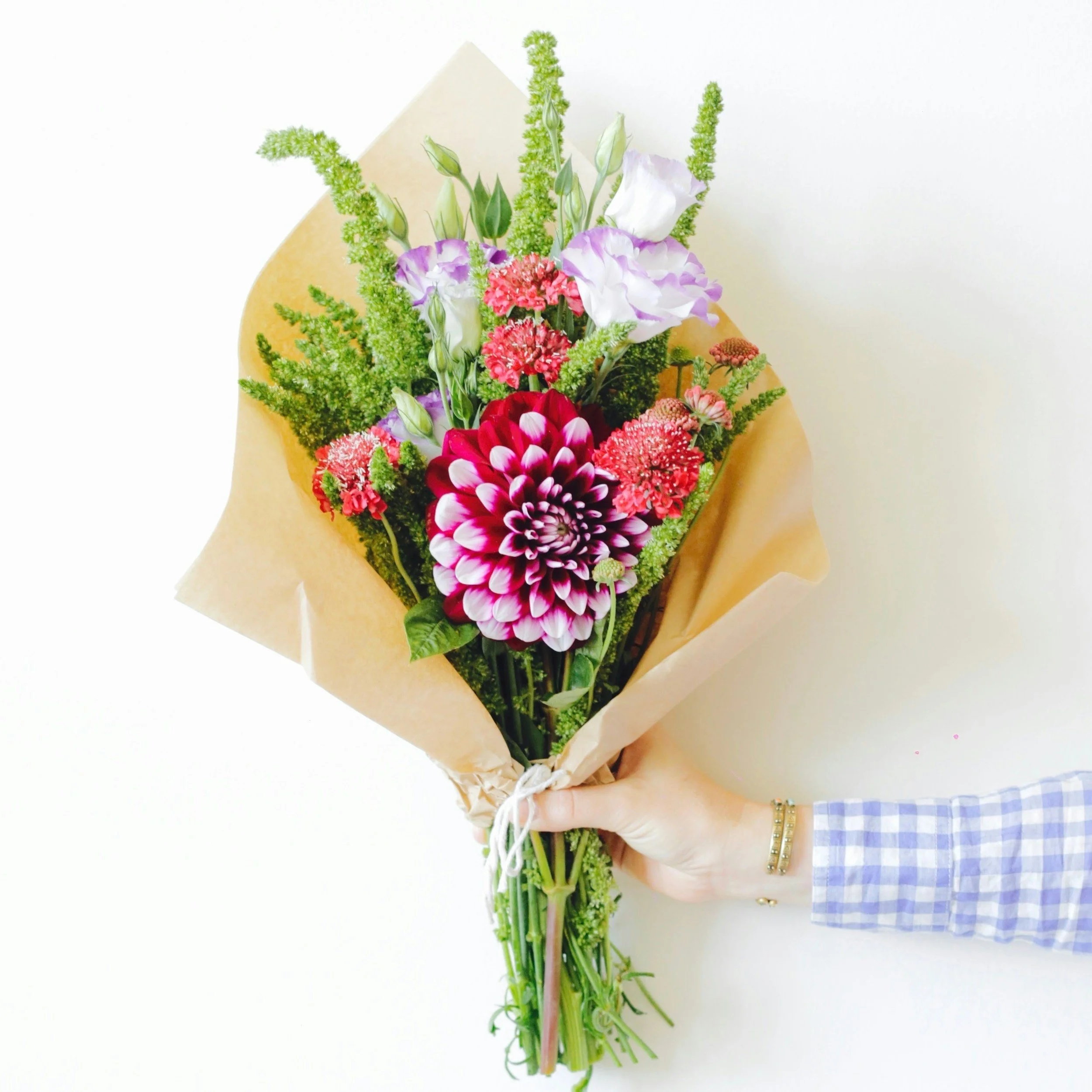 A hand holding a bouquet of various colorful flowers wrapped in kraft paper.