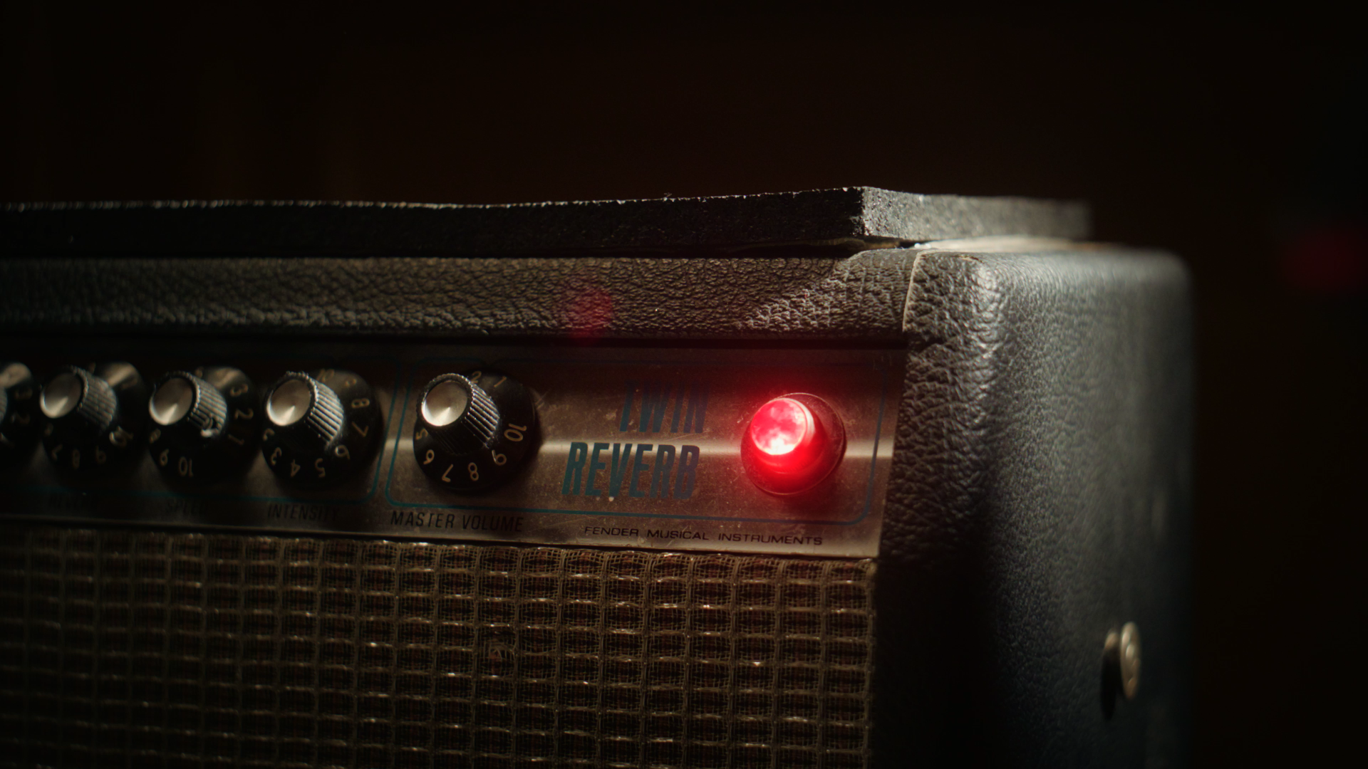 Close-up of a guitar amplifier with a red power indicator light, control knobs labeled for intensity and master volume, and a reverb effect panel with a textured black casing.
