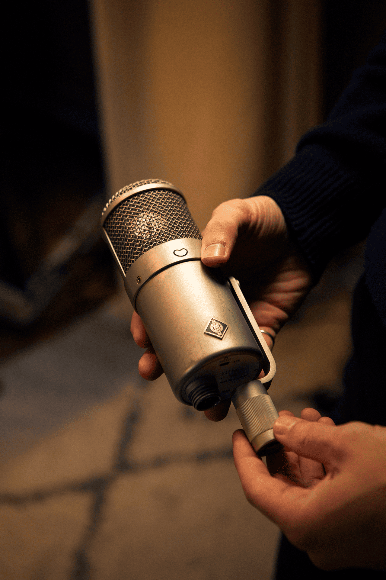 A person is holding a large, vintage-looking silver microphone with a gold-colored grille, adjusting its knob.