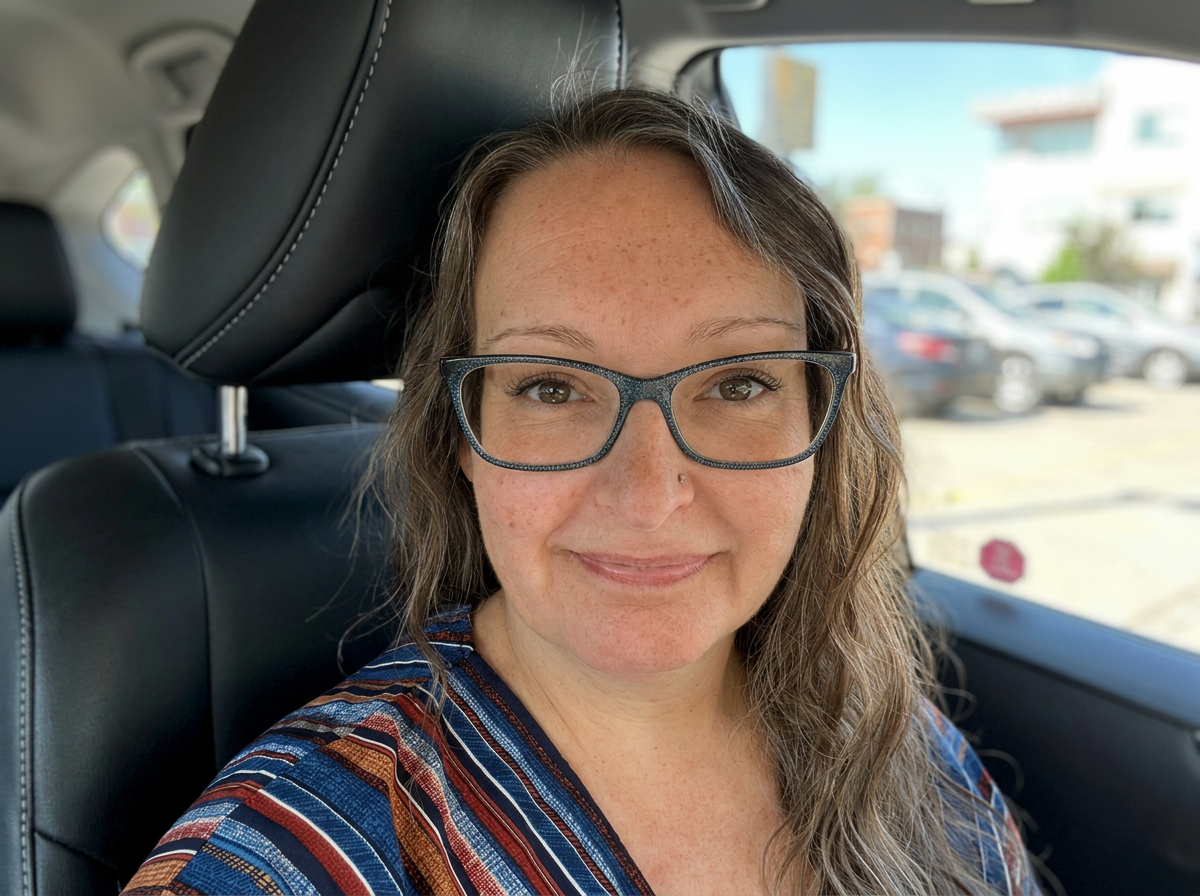 Woman with glasses and freckles smiling inside a car.