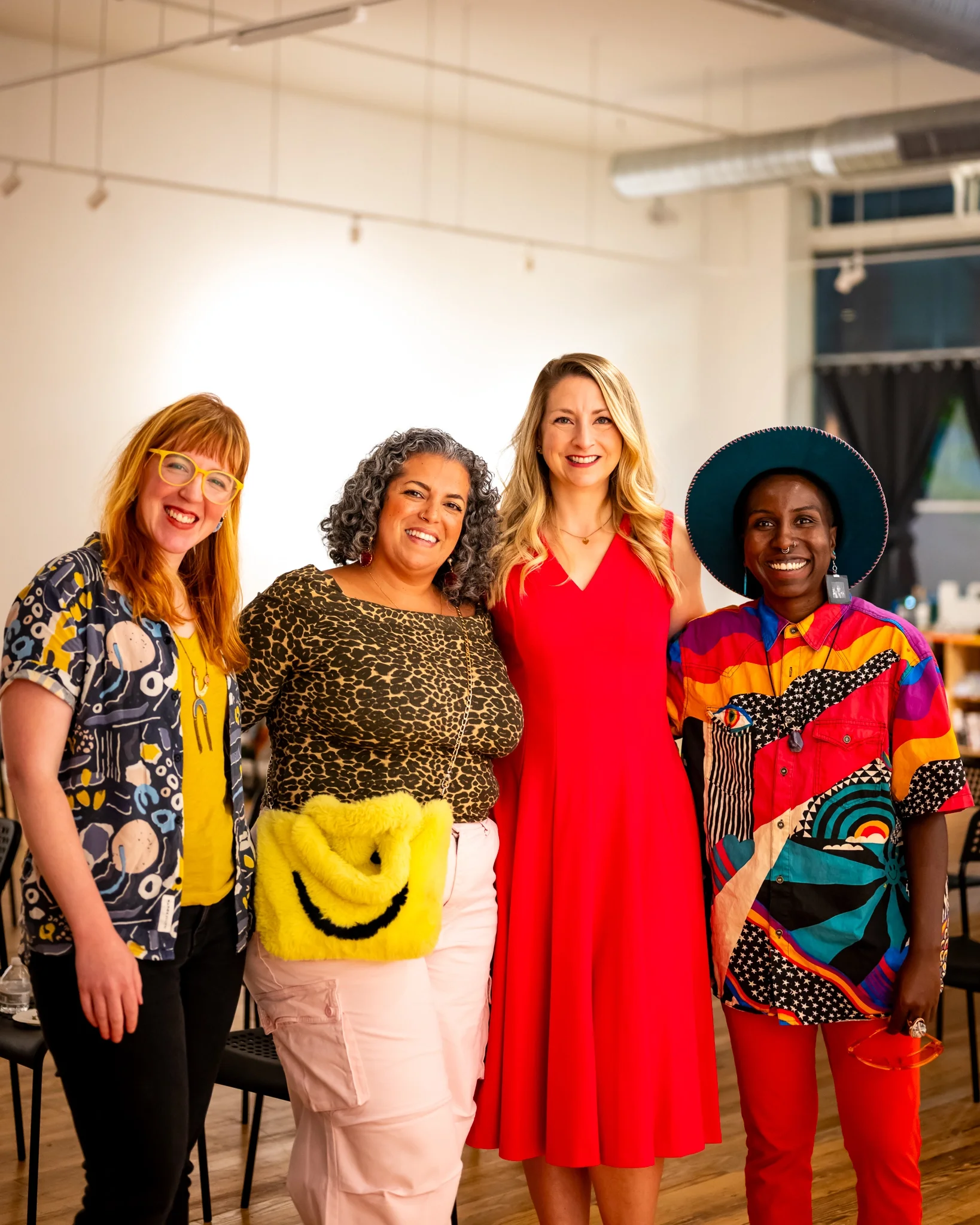 Four smiling people posing together at an arts event, one holding a yellow smiley-face purse.