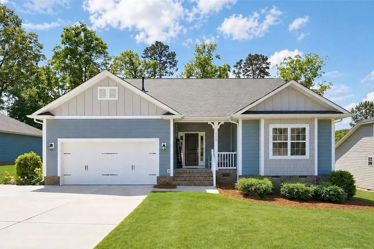 Front view of a blue house with a white garage door, small porch, and well-maintained lawn with bushes.