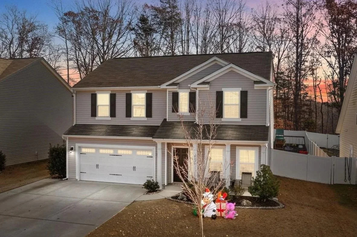 A two-story suburban house decorated for Christmas, with inflatable holiday figures like a snowman, a pig, and Santa, at sunset.