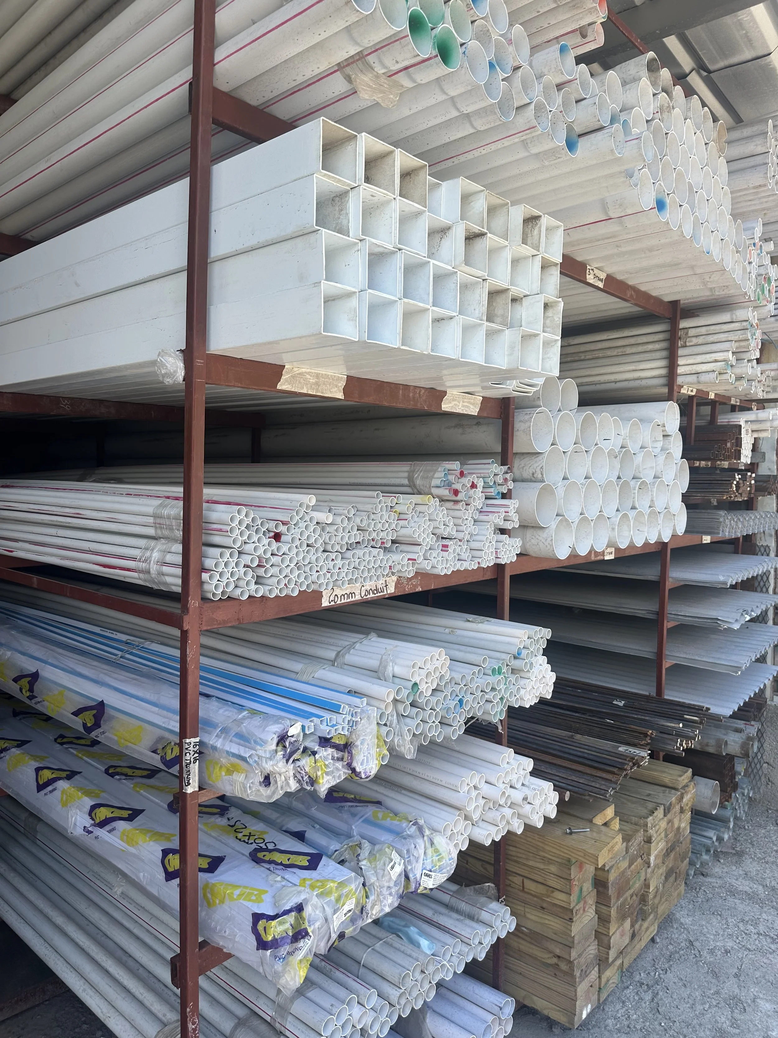 Shelves filled with various pipes and piping materials, including white, black, and colored pipes, at a hardware store.