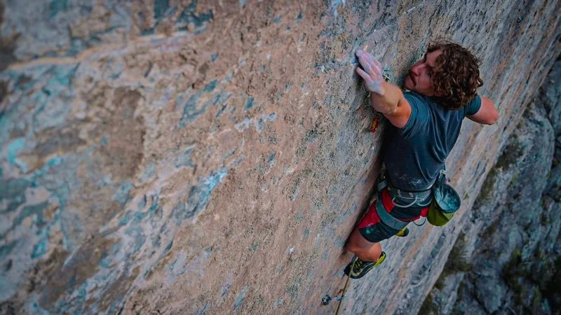 A person with curly hair rock climbing on a steep outdoor cliff.
