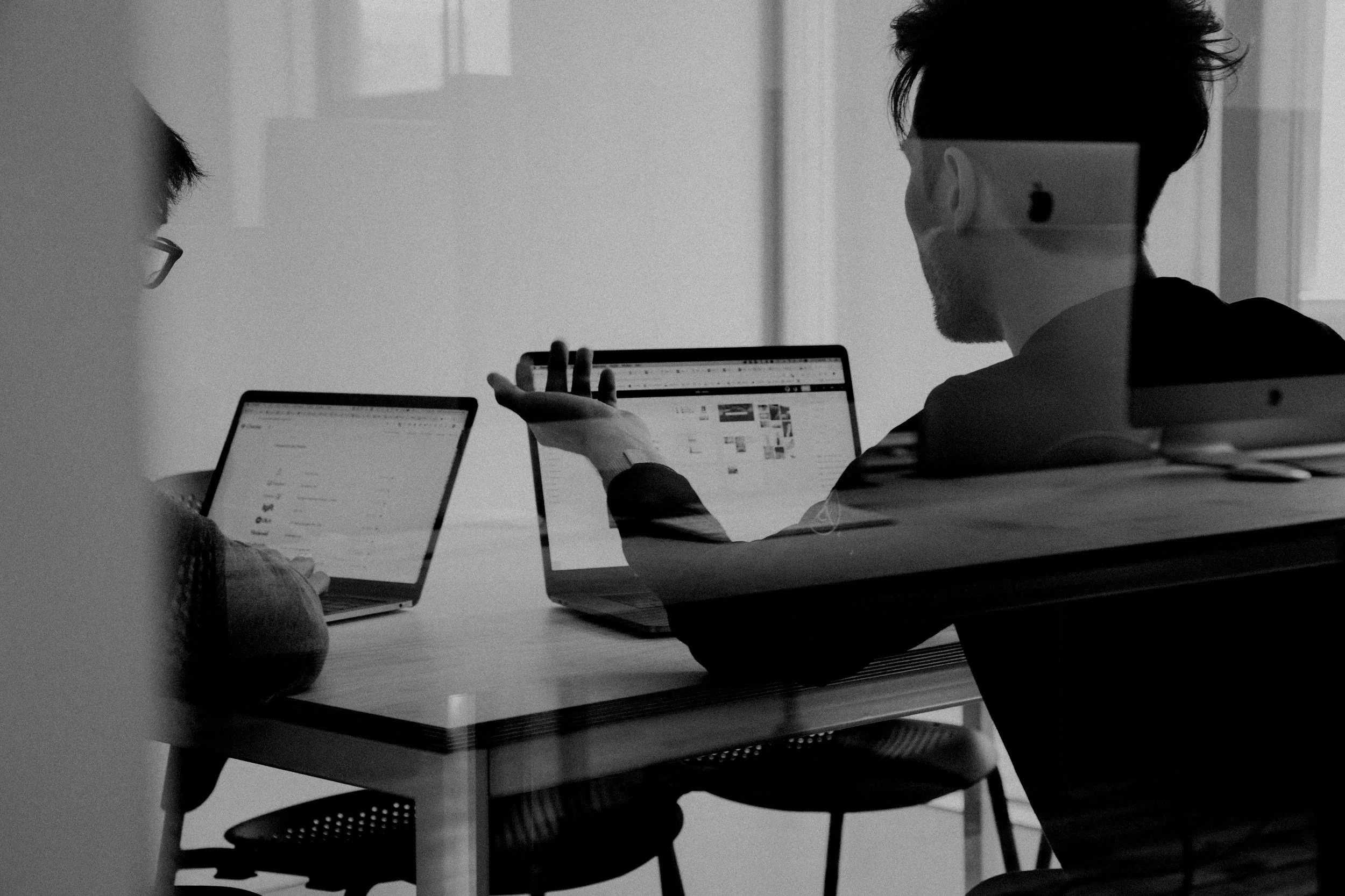 Deux personnes discutent du marketing numérique d'un client dans un espace de bureau ou de réunion, une utilise une tablette et l'autre un ordinateur portable.