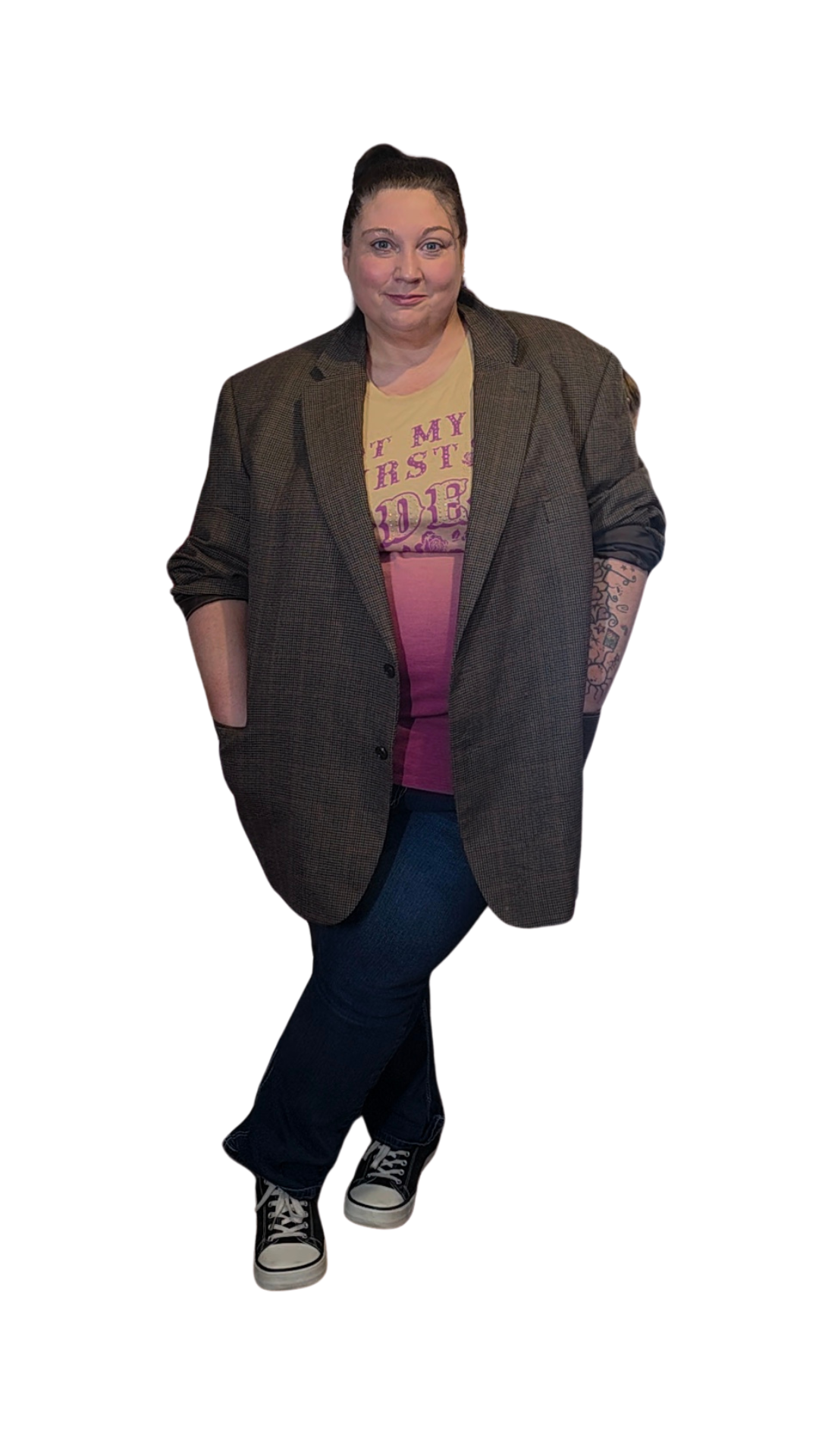 A woman with her hands in the pockets of a plaid blazer, wearing a yellow T-shirt with pink text, dark jeans, and sneakers, standing against a plain white background.