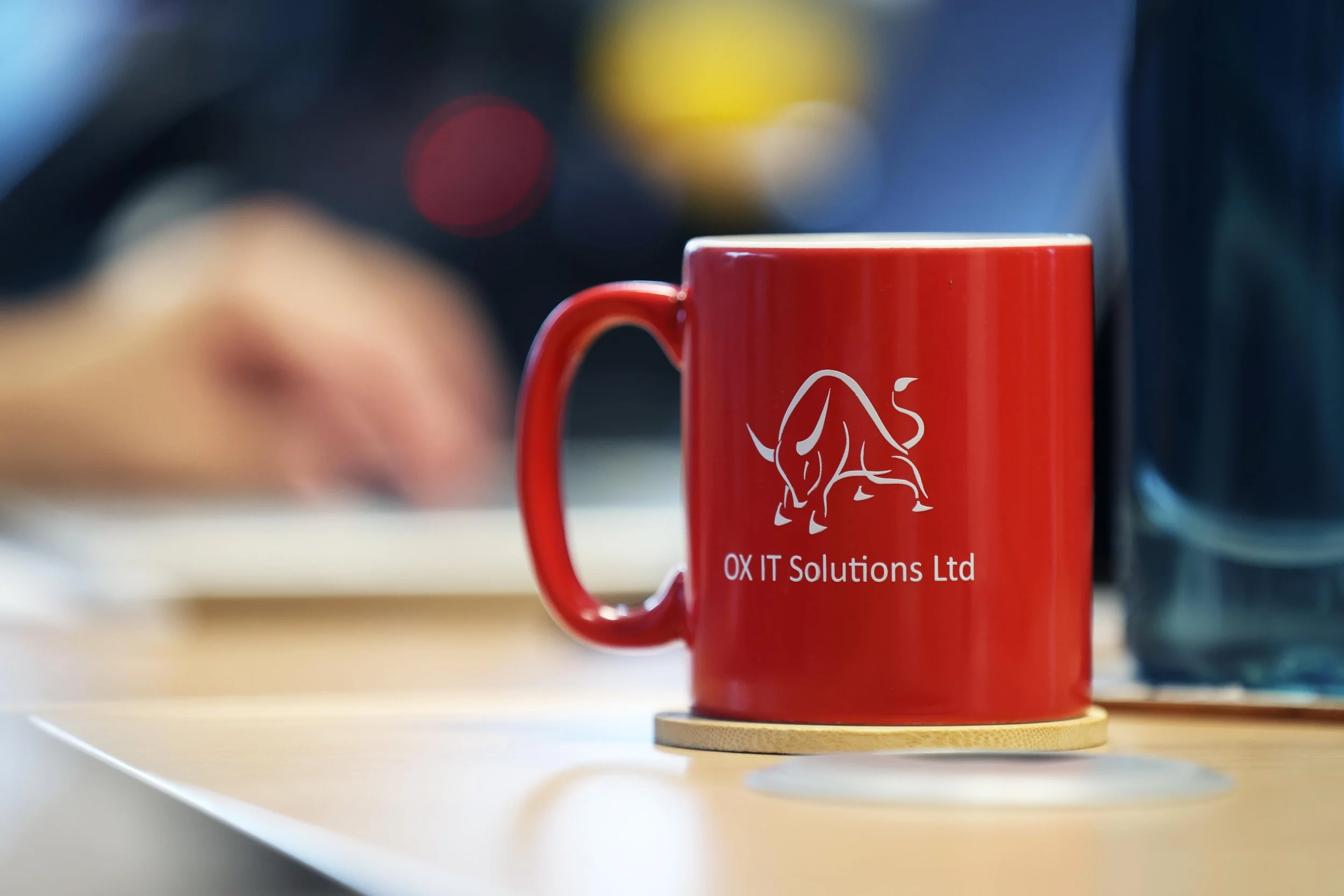 A red coffee mug on a table with a logo of a dog and the text 'OX IT Solutions Ltd'.