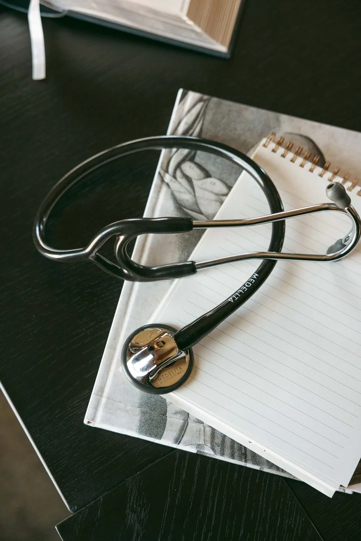 A stethoscope resting on a lined notebook, which is on top of a book or magazine, placed on a black surface.