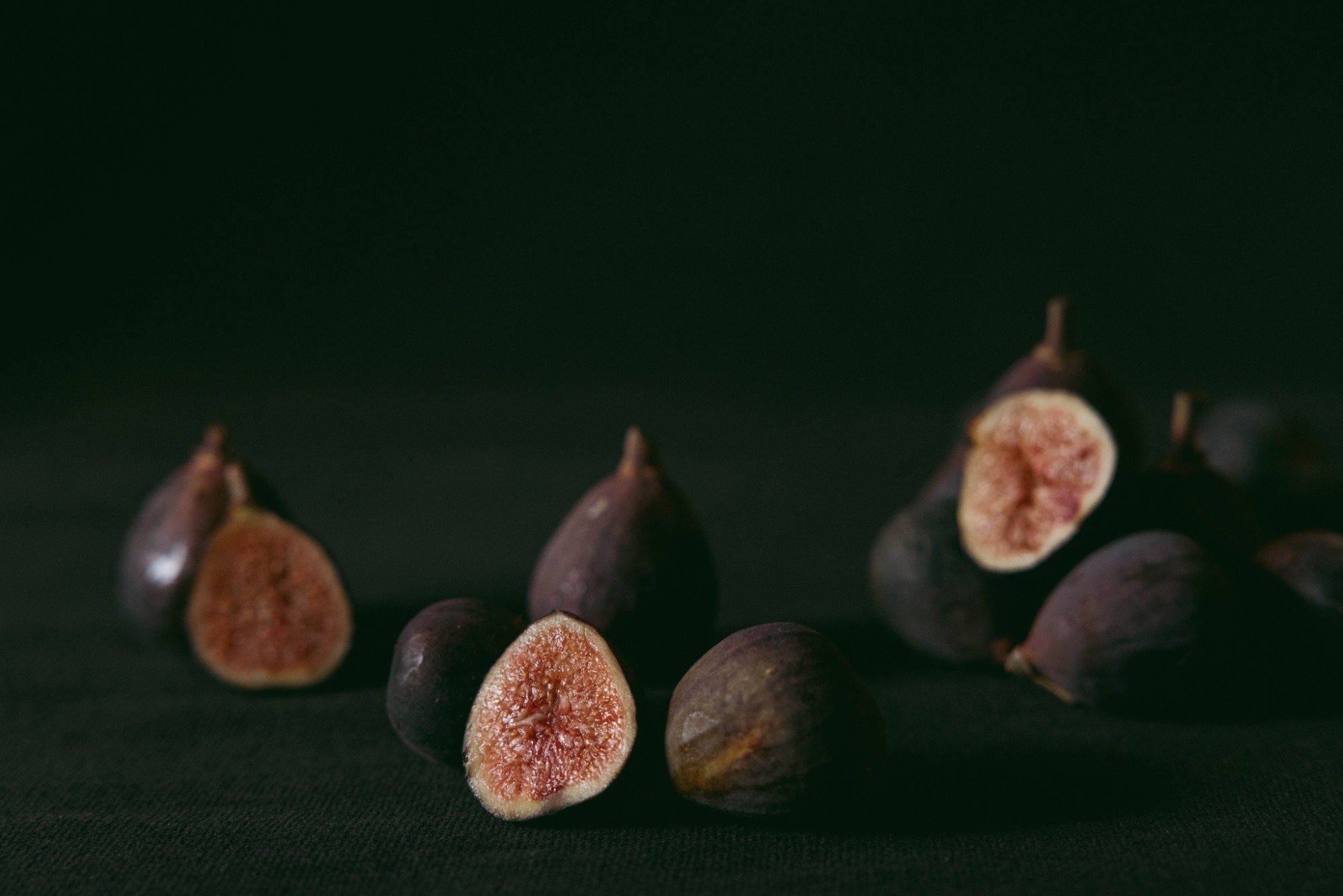 Close-up of halved figs with purple skin and pinkish-red flesh, arranged on a dark surface.