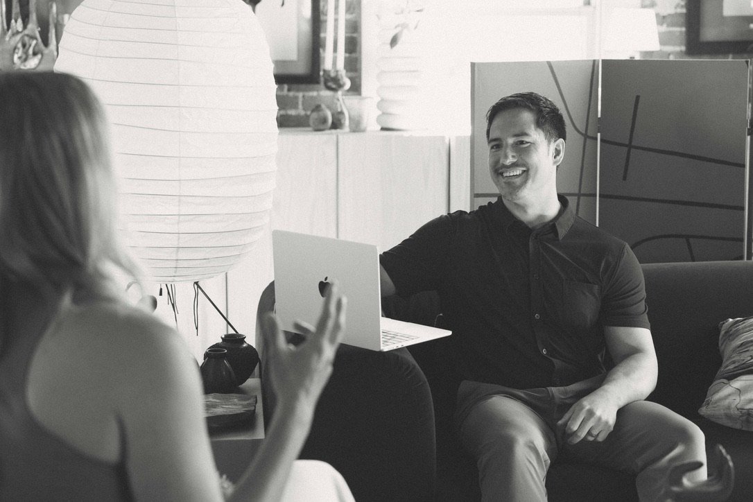 A man and woman engaged in a conversation in a modern, well-lit indoor space, with the man smiling and the woman gesturing.