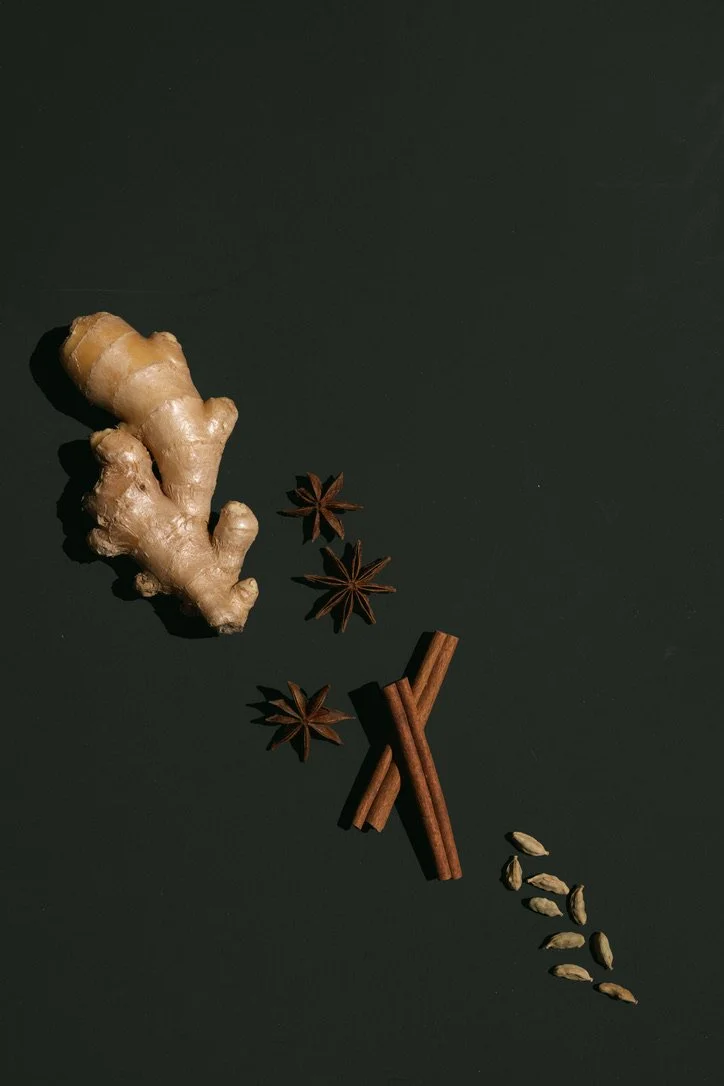 Ginger root, star anise, cinnamon sticks, and cardamom pods arranged on a dark surface.