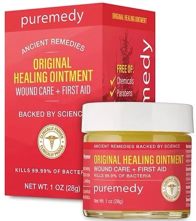 A red and white box and a small jar of Puremedy's Original Healing Ointment, with the box standing behind the jar. The box features text about the ointment's benefits, ingredients, and scientific backing.