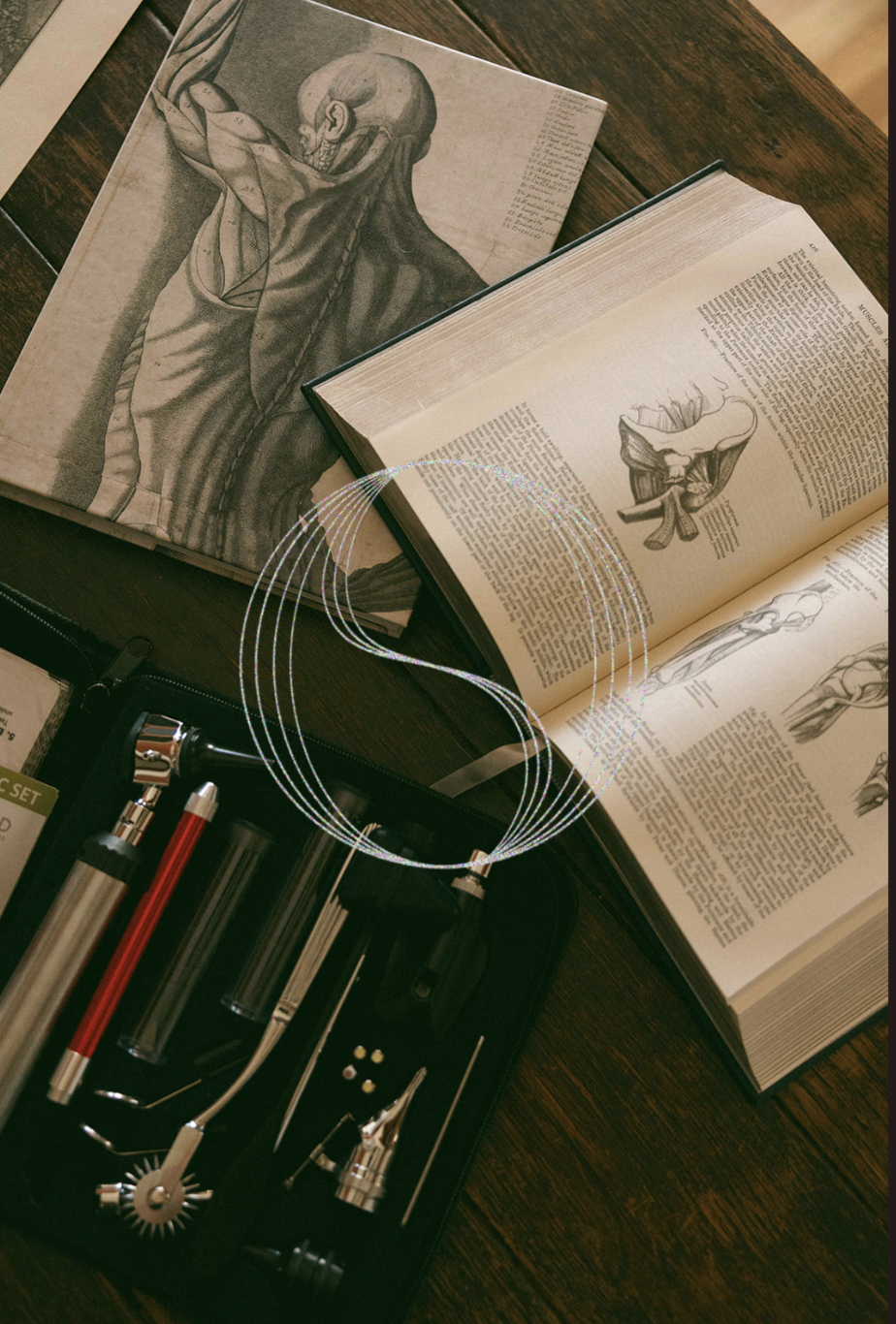 Open anatomy books showing illustrations of the human muscular system, alongside a scientific tool kit with various instruments, on a wooden surface.