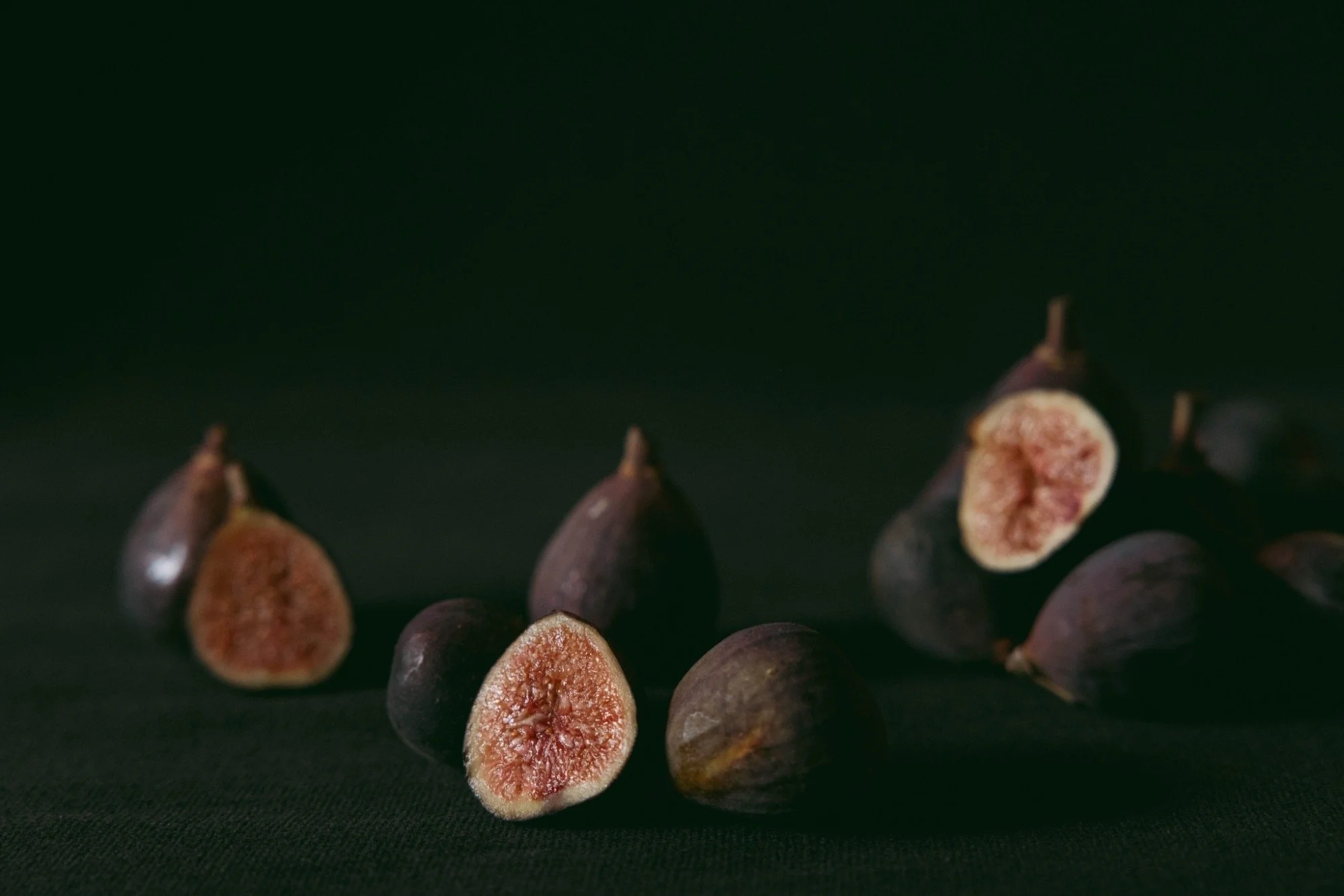 Close-up of several fresh figs, some whole and some cut in half, against a dark background.
