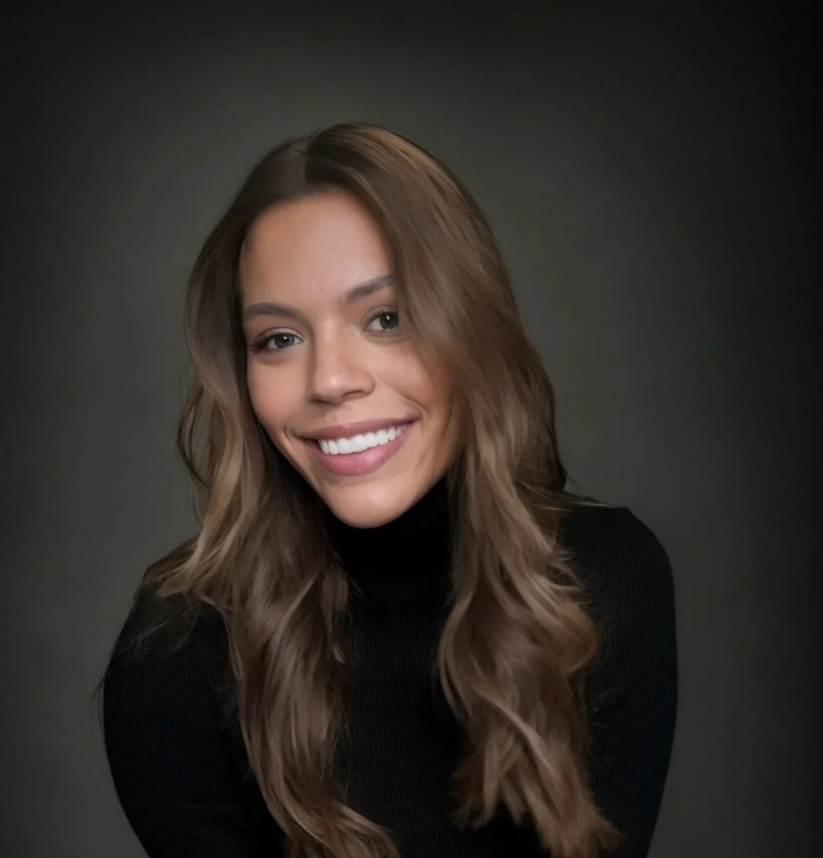 A young woman with long, wavy brown hair and a black turtleneck, smiling at the camera against a dark background.