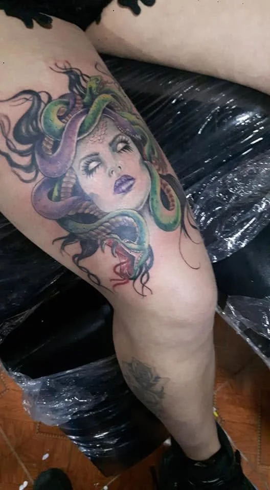 Tattoo of a woman's face with snakes as hair on person's thigh.