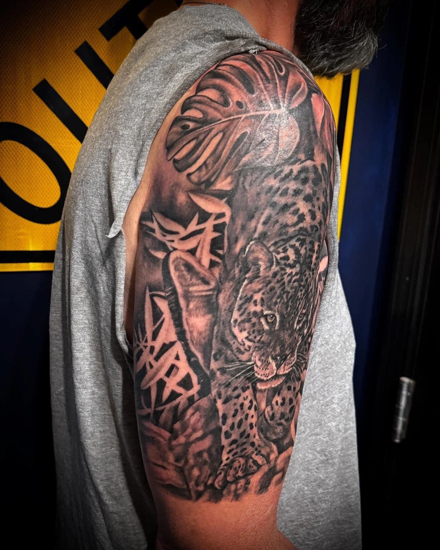 Tattoo sleeve on a person's upper arm featuring a realistic leopard's face with detailed fur, piercing eyes, and surrounding tribal-style patterns.