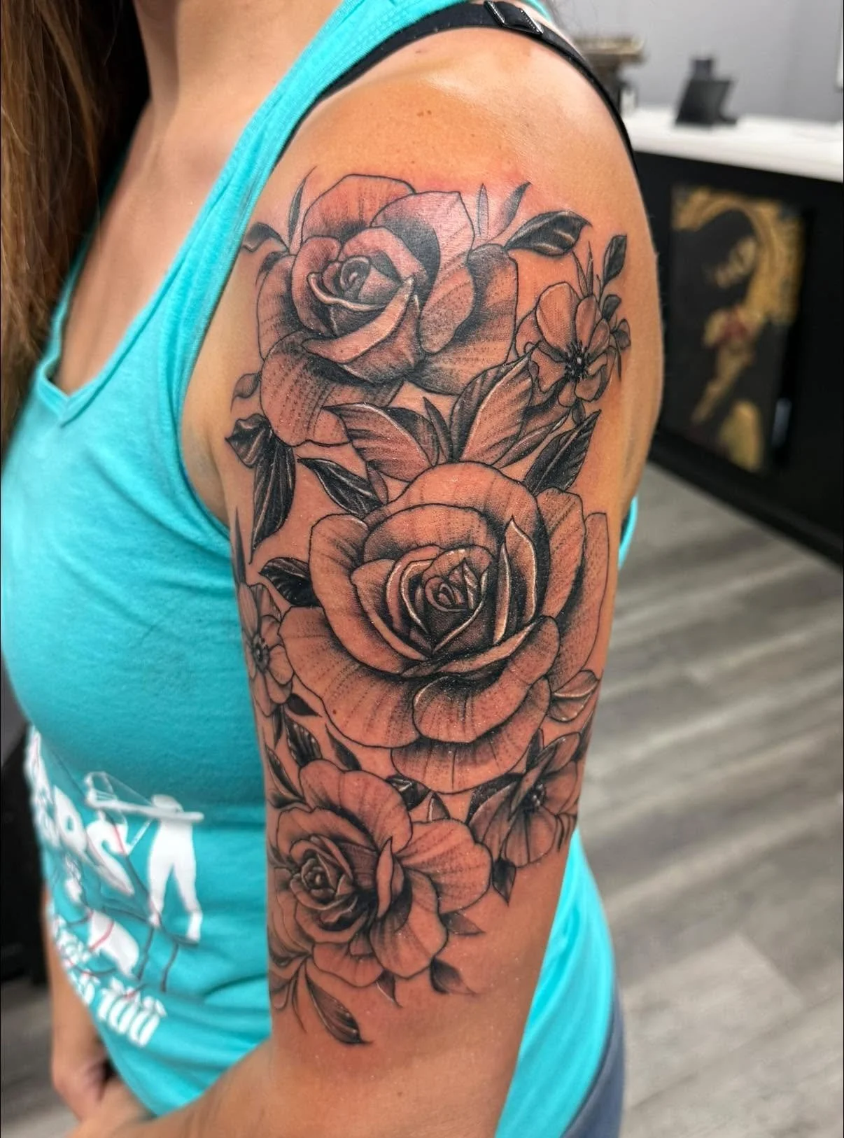 A black and gray tattoo of several large roses and leaves on a person's upper arm and shoulder.