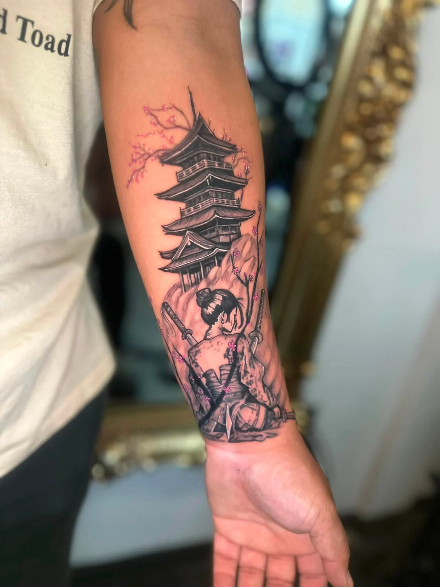 Tattoo of a traditional Japanese pagoda with pink cherry blossoms on a person's forearm.