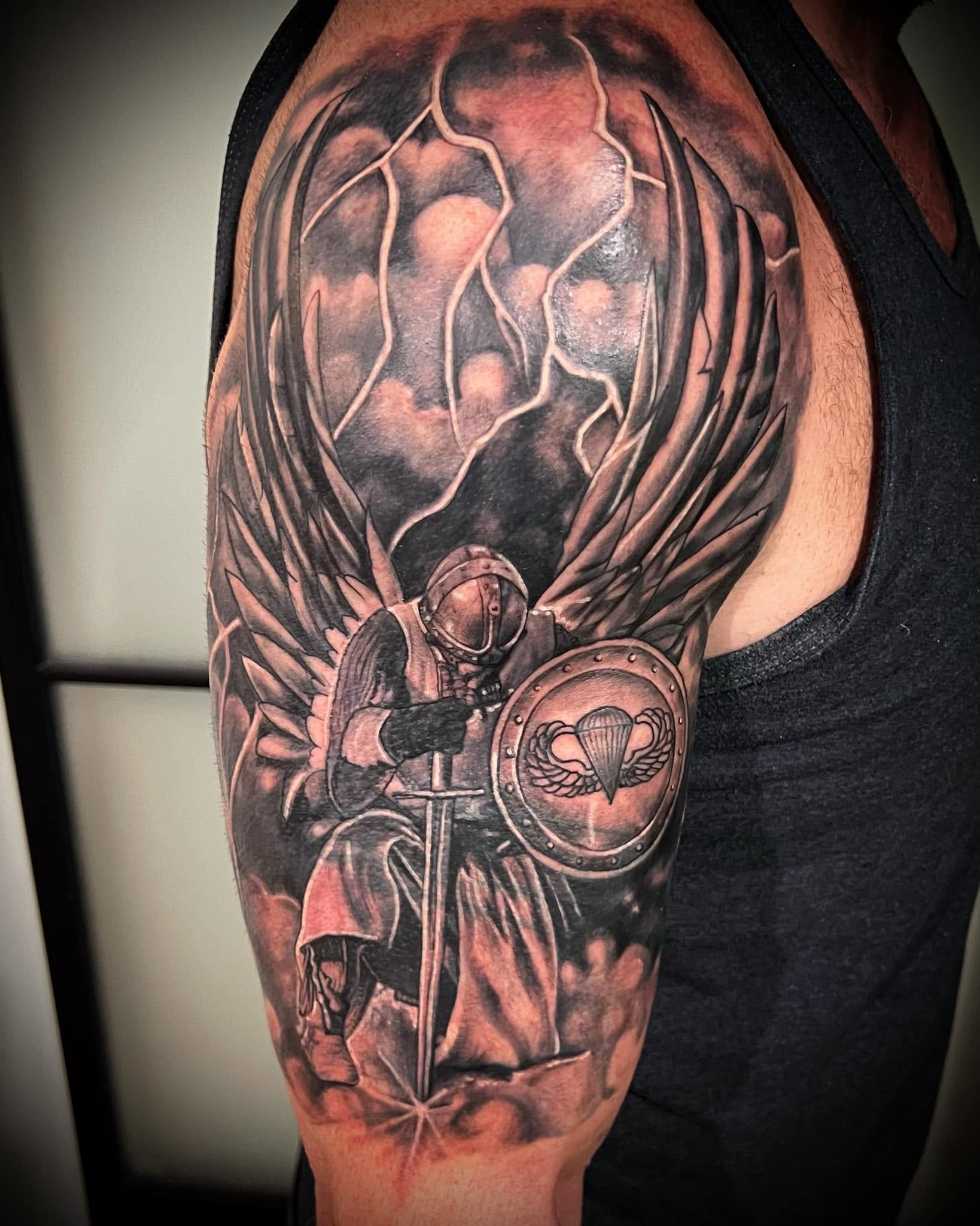 Close-up of a person's upper arm with a detailed black and gray tattoo featuring various designs, including a skull, tentacle, and a badge with an eagle.