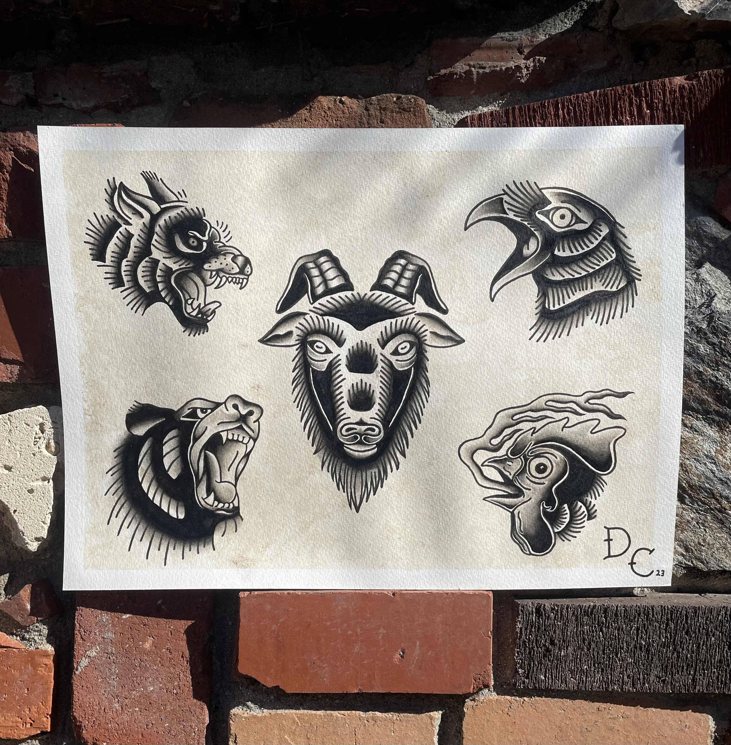 Black and white tattoo-style illustration of a lion, a eagle, and a wolf on a piece of paper against brick and mortar background.